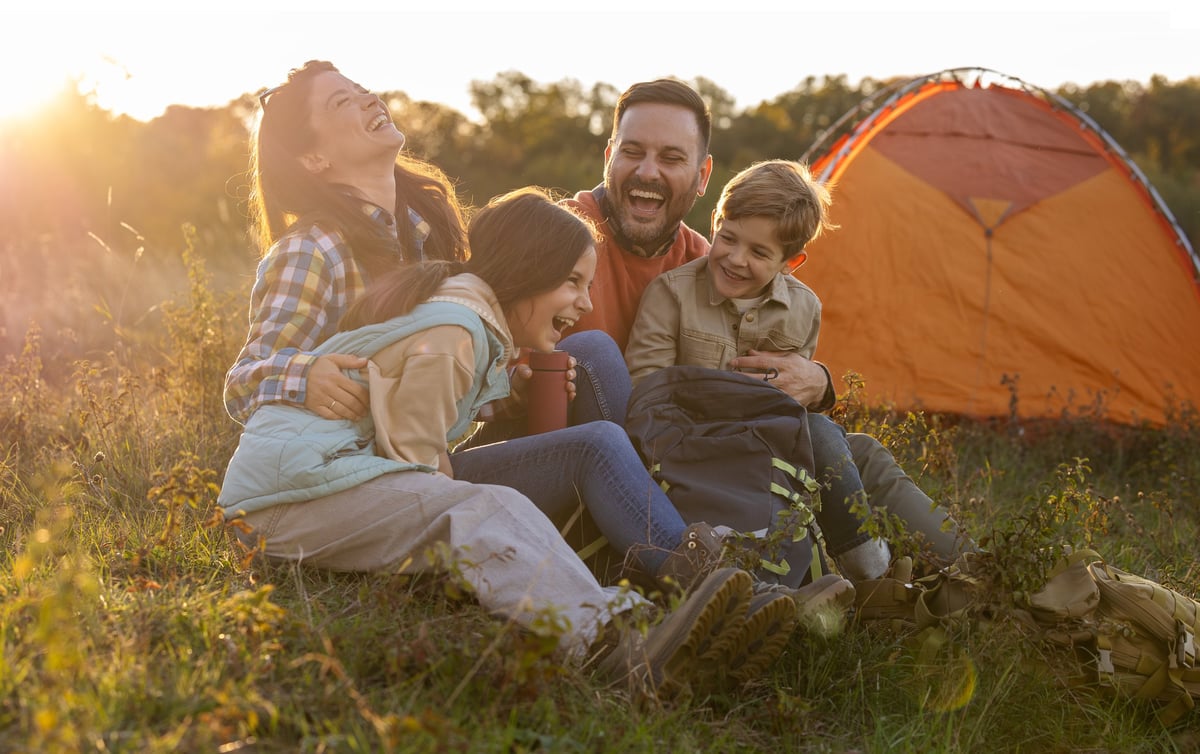 Family of four laughing near their tent at sunset
